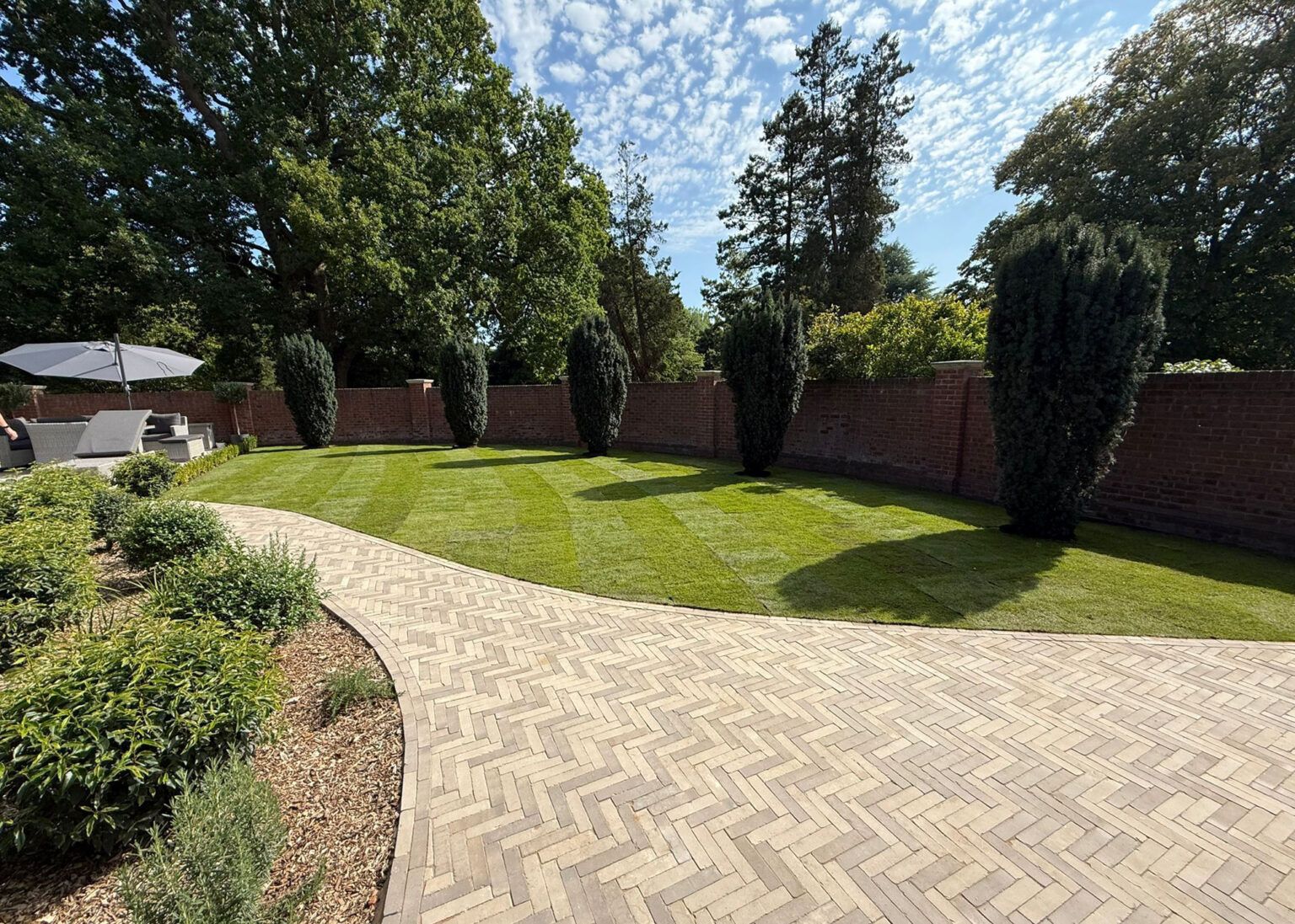 Curved lawn with herringbone brick pathway and formal planting design